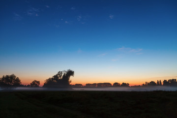 Fototapeta na wymiar Evening mist on meadow at sunset, silhouette trees