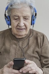 senior woman listening music with headphones and smart phone