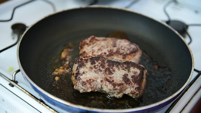 Beef ribeye steak being fried in a pan on the stove