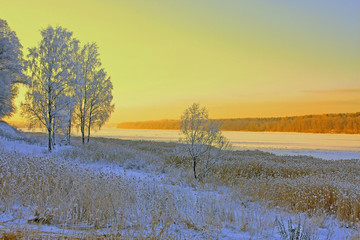 beautiful winter landscape at sunset with river and snow-covered trees