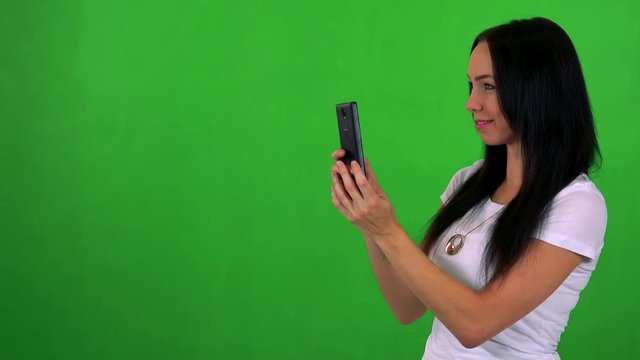 young pretty woman takes photos wirh smartphone - green screen - studio 