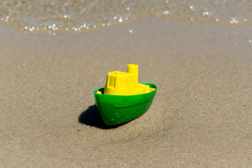 Fototapeta na wymiar Toy boat in the wet sand of the sea. Summer holidays at sea. Boat trips.