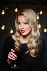 Beautiful blonde girl in evening dress smiling, holding wine glass.