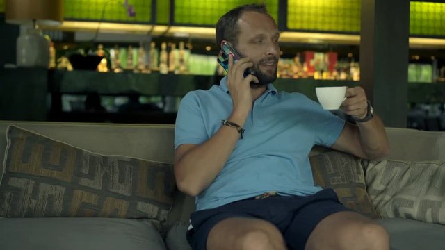 Happy attractive man talking on cellphone and drinking tea in cafe, 4K

