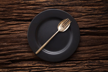 black empty plate fork spoon on wooden table background