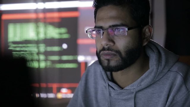 Male hacker hacks computer in dark. Computer code reflecting on his face. HD.