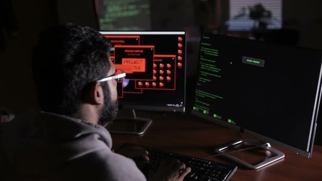 Male hacker hacks computer in dark. Computer code reflecting on his face. HD.