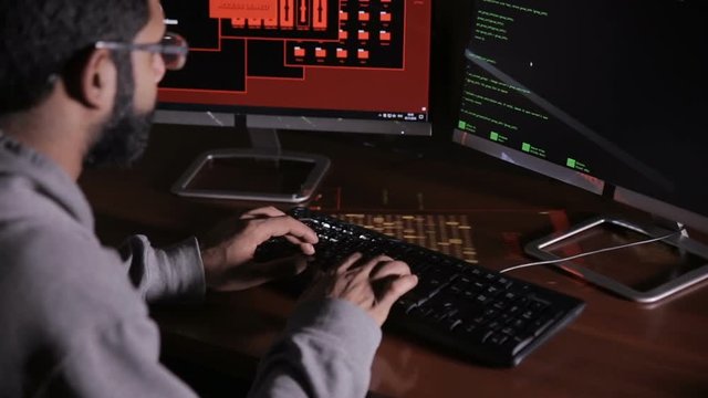 Male hacker hacks computer in dark. Computer code reflecting on his face. HD.