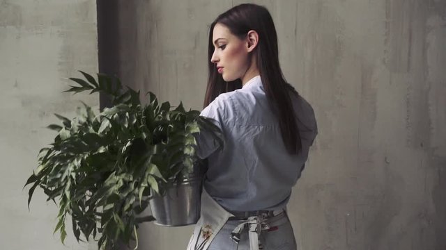 Florist workspace: young pretty caucasian woman making floral decorations, a bunch of green leaves in her hands.