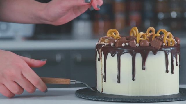 Slice of chocolate cream brownie cake topped with white chocolate. Female hands cut homemade cake. Girl makes cake, cutting shortcake into two layers. Cutting chocolate cake.