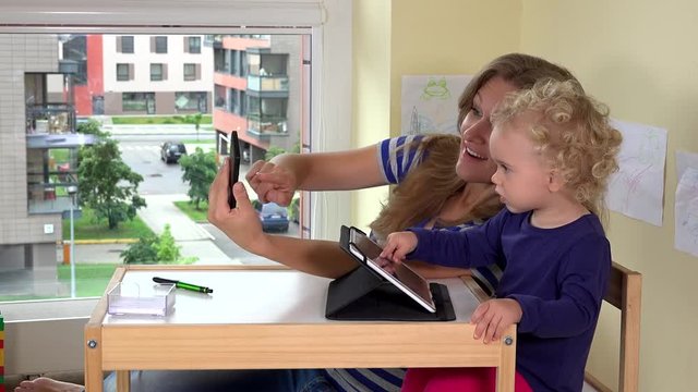 Mother with child shoot selfie photographs with smartphone.