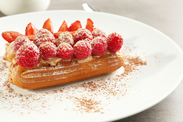 Delicious eclairs with berries, ground cinnamon and sugar powder on white plate