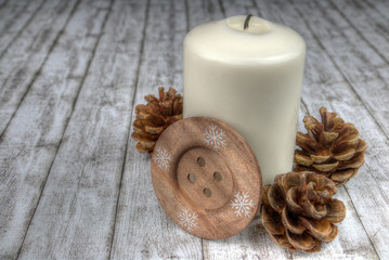Dekoration - angebrannte weiße Kerze mit Tannenzapfen und braunem Knopf auf weißem Holz