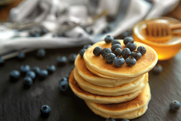 Stack of delicious pancakes with blueberries and honey on slate