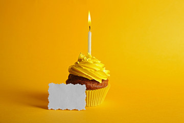 Fresh tasty cupcake with candle and birthday card on yellow background