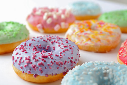 Tasty donuts with colorful sprinkles on light background