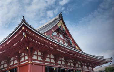 Tokyo, Japan - September 26, 2016: Part of the highly decorated vermilion roof of the Honzo main hall at Senso-ji Buddhist Temple under blue cloudy sky. Gold metalic decorations.