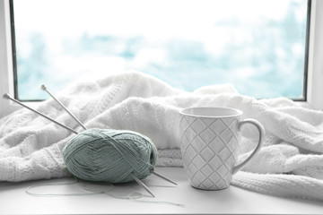 Hot drink with threads and plaid on windowsill