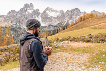 Bearded hiking man in Alps mountains drinking tea or coffee and enjoying amazing view of autumn nature. Traveler warming his hands with mug of tea. Alps Austria Europe at fall season. 