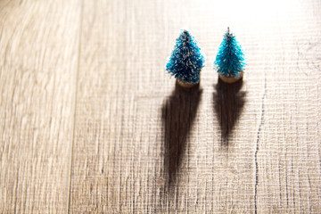 two small artificial Christmas trees throw a shadow on wooden background, there is a place for the text as the substrate. the view from the top
