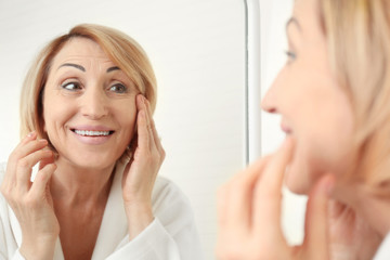 Obraz na płótnie Canvas Senior woman doing facial anti aging massage near mirror