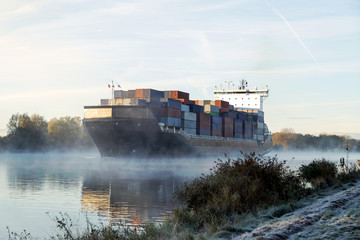 Containerschiff im herbstlichen Morgennebel auf dem Nord-Ostsee-Kanal bei Sonnenaufgang