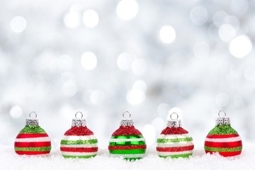 Red, green and white Christmas ornaments in snow with twinkling silver background
