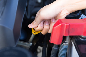 Asian woman's hand checking level of lubricant oil of car engine.