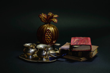 Still life with old books, pomegranate and small cups on a black background. Light painting.