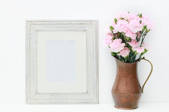 An empty white frame and a copper vase with miniature pink carnations on a white isolated background for adding text or a photo to use as a mock up for a business plan concept.
