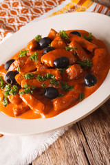 Spanish pork Raxo in a sauce of wine, tomatoes and cream with black olives close-up. vertical