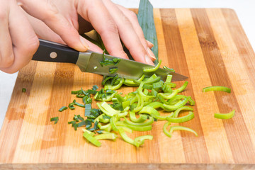 Woman's hand with a knife cuts the leek on the wooden board in the kitchen. Healthy eating and lifestyle.