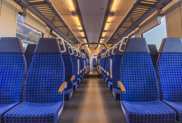 Fototapeta premium Puste krzesła w pociągu - obraz przedstawiający wnętrze nowoczesnego niemieckiego pociągu bez ludzi na niebieskich krzesłach