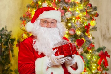 Fototapeta na wymiar Santa Claus with giftbox on background of sparkling firtree