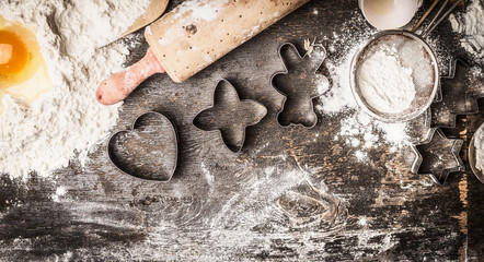 Christmas baking: flour, egg yolk, rolling pin, cookie cutters on dark wooden background, top view, border