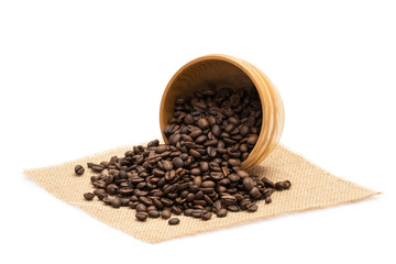 Roasted coffee beans with an overturned wooden bowl on a piece of sack cloth with white background