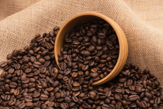 Roasted coffee beans with an overturned wooden bowl on sack cloth