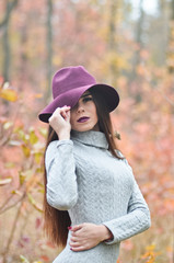 Long-haired girl in a burgundy hat in the middle of autumn forest.
