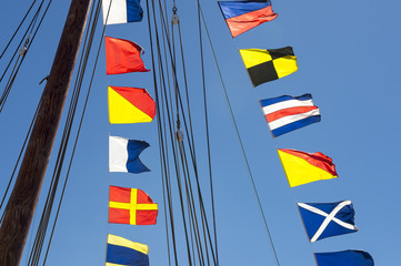 Fototapeta premium Colorful nautical sailing flags flying in the wind from the lines of a sailboat mast backlit in bright blue sky by the sun
