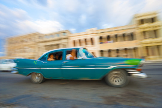 Vintage taxi driving in front of classic colonial architecture on the Malecon in Central Havana, Cuba