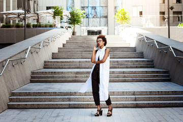 Young beautiful african girl speaking on phone walking down city.