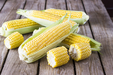 A whole fresh corn and pieces of corn on the wooden table