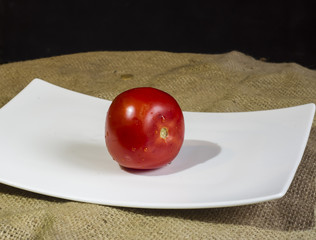 czerwony dojrzały pomidor na białym talerzu na stole, warzywo
