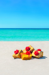 Gift boxes with big red bows on sandy sunny beach