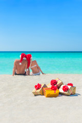 Golgen gifts and couple in Christmas Santa hats at beach