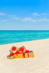 Golden wrapped fancy boxes with bows at tropical ocean beach