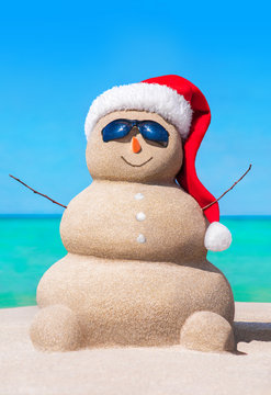 Sandy snowman in Christmas hat and sunglasses at tropical beach