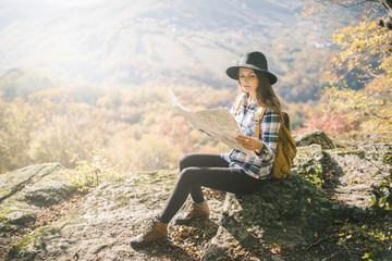 Young hipster woman sitting at viewpoint and looking at map for direction