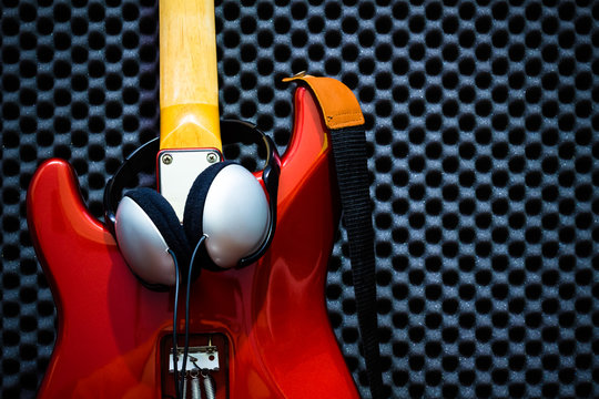 headphone on back of red electric guitar, acoustic board background