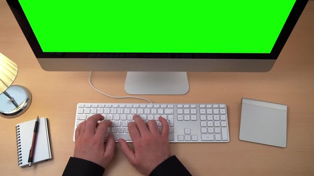 static shot of a man in his home office typing on a keyboard in front of a green screen computer display